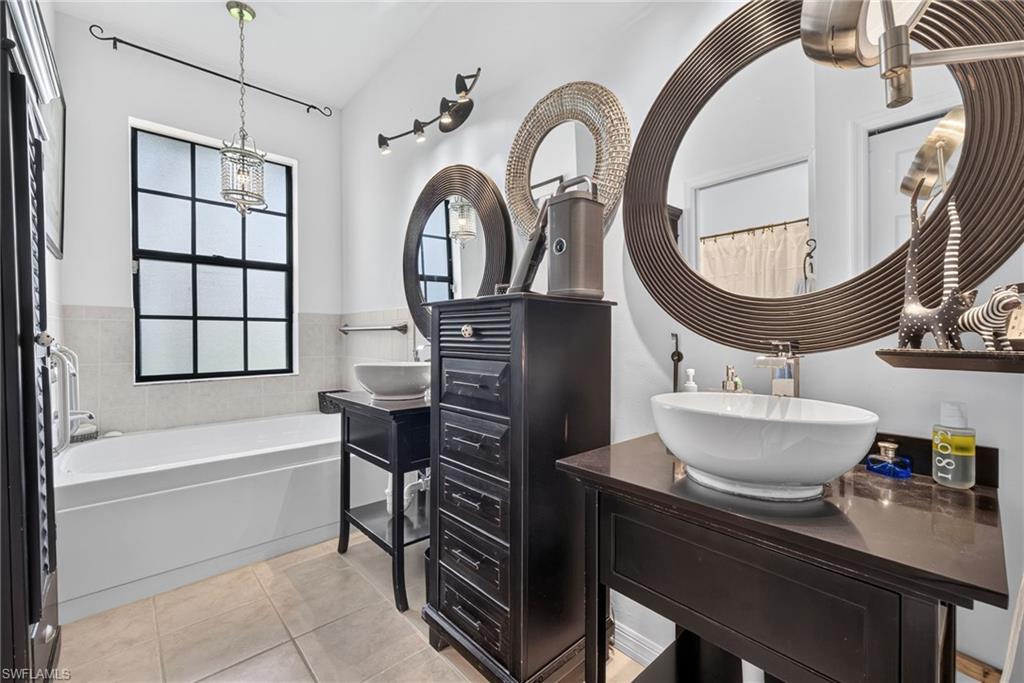 Bathroom featuring a built-in soaking tub, a window with grid detailing, two vessel sinks, and tile flooring