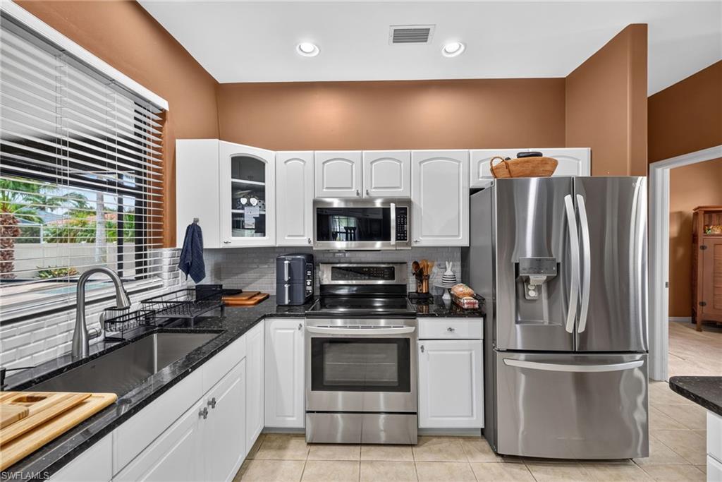 Kitchen featuring white cabinetry, dark granite countertops, stainless steel appliances, and a tile backsplash