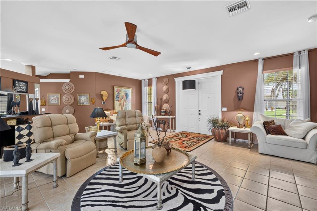 Living area featuring neutral-toned tile flooring, a wood-finish ceiling fan, and double entry doors with white trim