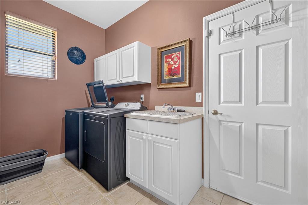 Laundry room featuring tile flooring, a utility sink with a countertop, white cabinetry, and a window with blinds