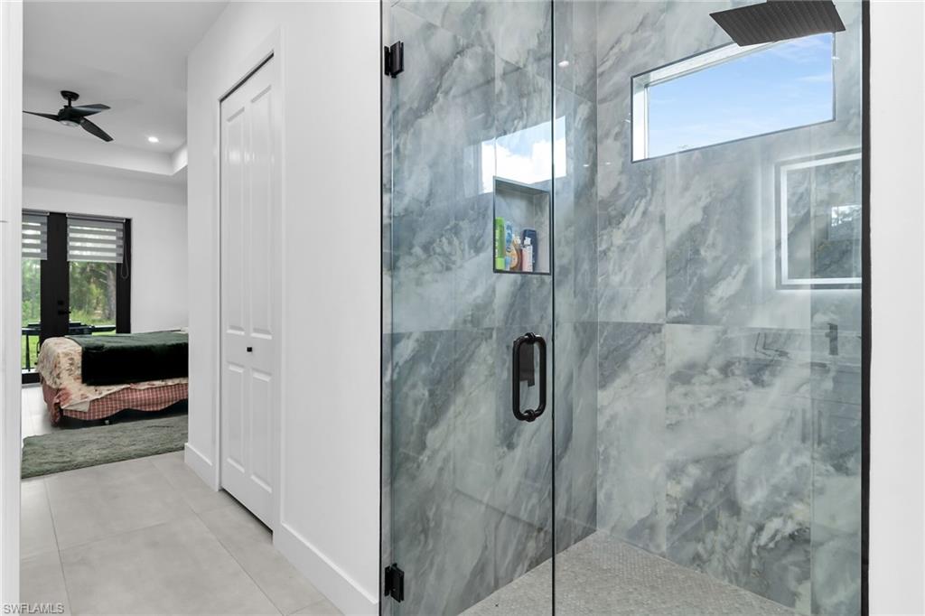 Glass-enclosed shower with large format marble-look tile, rainfall showerhead, and integrated shelving niche