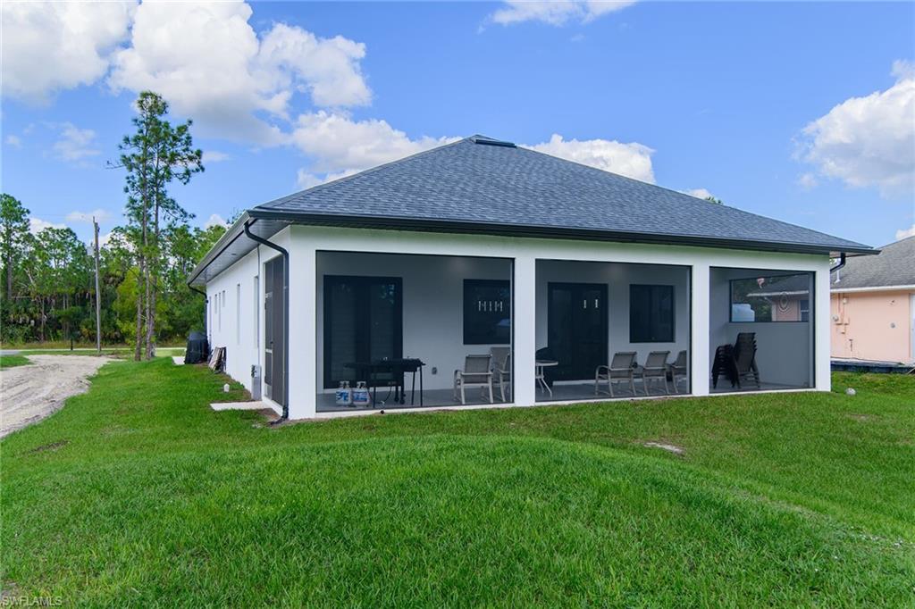 Rear exterior featuring a screened patio with a dark grey shingle roof and white stucco siding