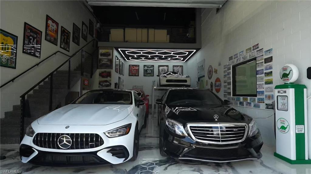 Two-story garage featuring polished concrete flooring with a hexagonal tile pattern, a black metal staircase, white block walls, and a dedicated mezzanine level