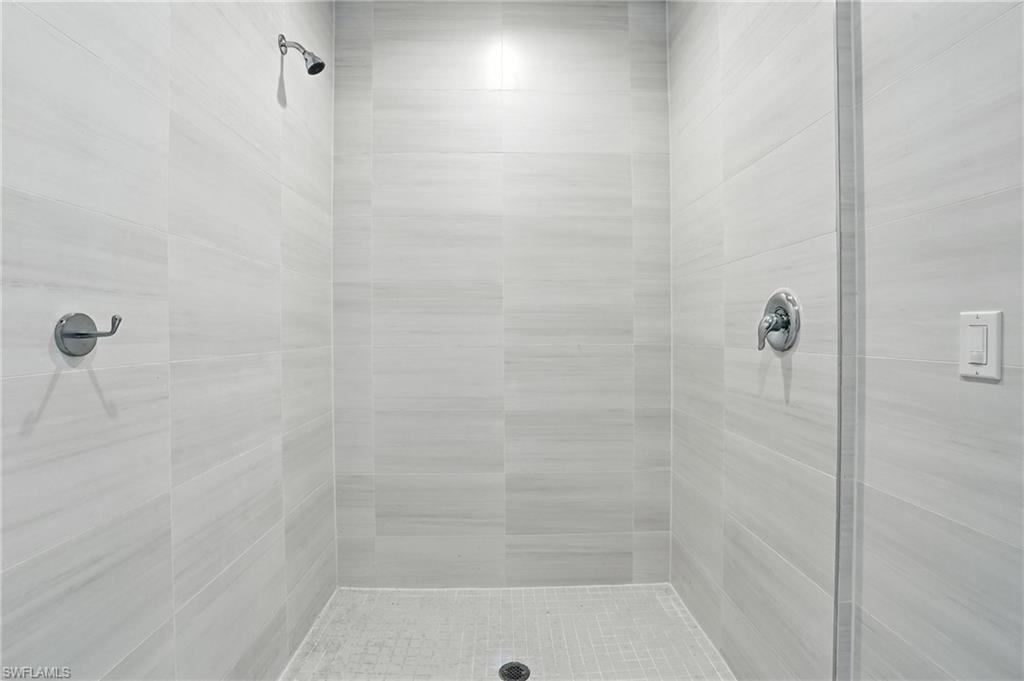 Shower enclosure featuring light grey rectangular wall tiles with subtle horizontal veining, a chrome shower head, a chrome temperature control, and a tiled shower pan