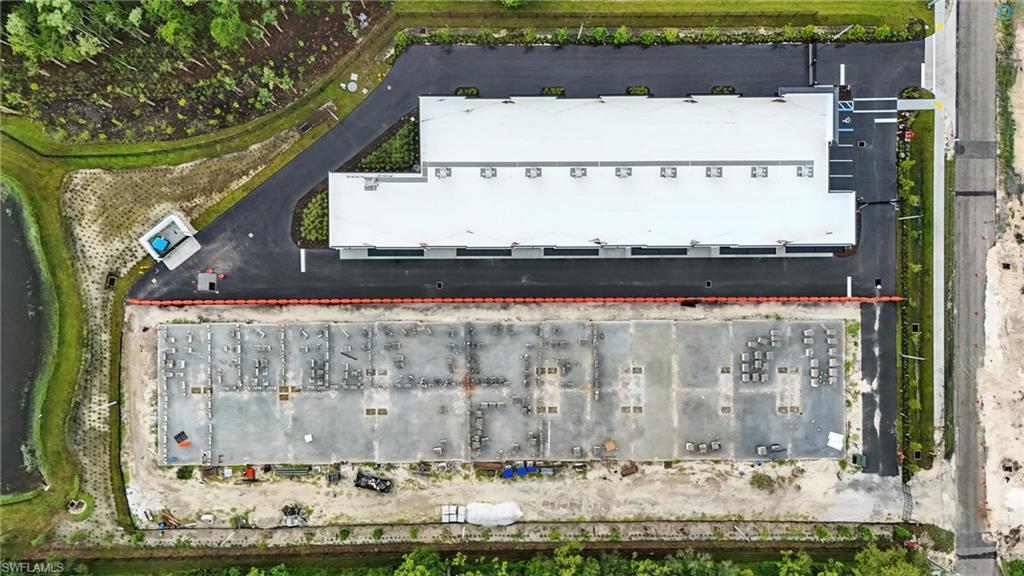Expansive commercial property featuring a completed building with a white roof and extensive paved parking areas