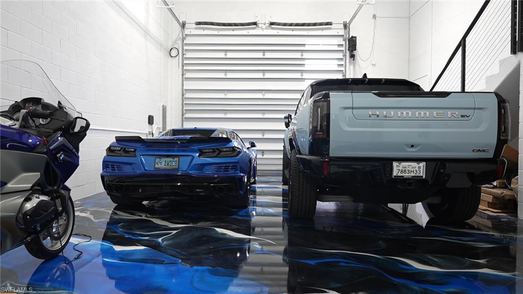 Spacious garage featuring an overhead roll-up door, polished concrete flooring with a blue and black finish, white painted brick walls, and integrated overhead lighting