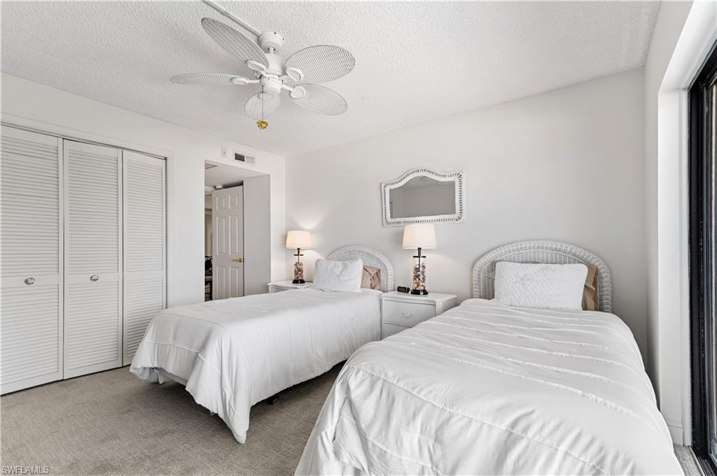 Room featuring two beds with wicker headboards, carpet flooring, a ceiling fan, and louvered bifold closet doors