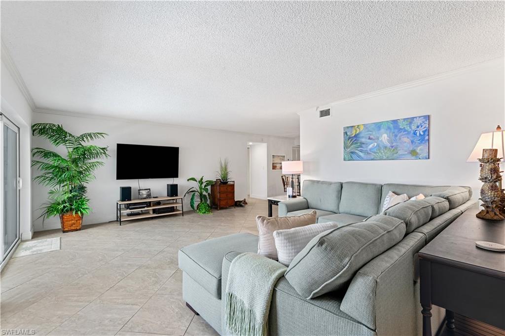 Spacious living area featuring neutral tile flooring, crown molding, and sliding glass doors