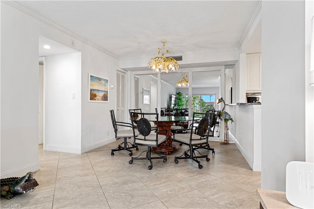 Spacious dining area featuring tile flooring, crown molding, a decorative chandelier, and a pass-through counter with a stone surface