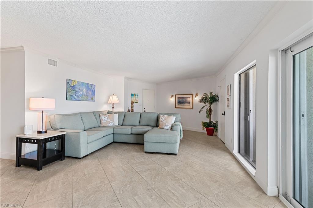 Spacious living area featuring light-toned tile flooring, white walls, and crown molding