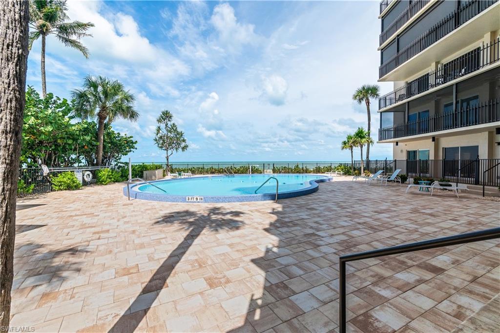 Resort-style pool area featuring a freeform swimming pool with blue tile surround, expansive paver patio, lush tropical landscaping, and immediate proximity to the ocean