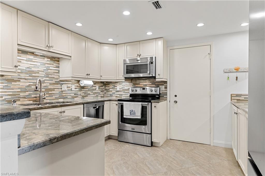 Kitchen featuring light-toned cabinetry, stainless steel appliances, a multi-tone tile backsplash, and granite countertops