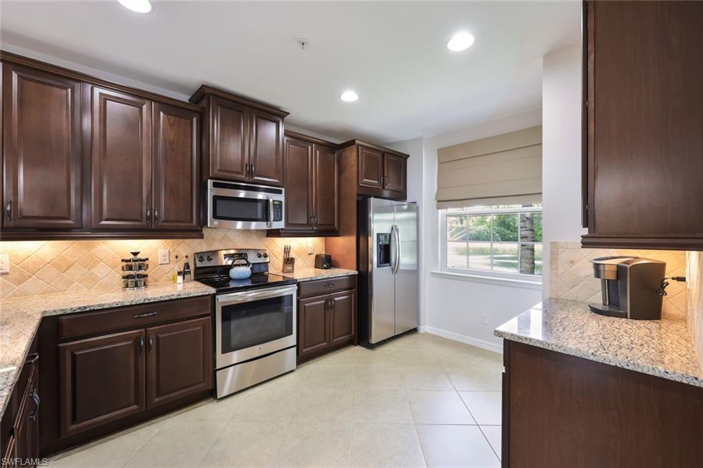 Kitchen with dark brown cabinets, light tile patterned floors, light stone counters, appliances with stainless steel finishes, and decorative backsplash