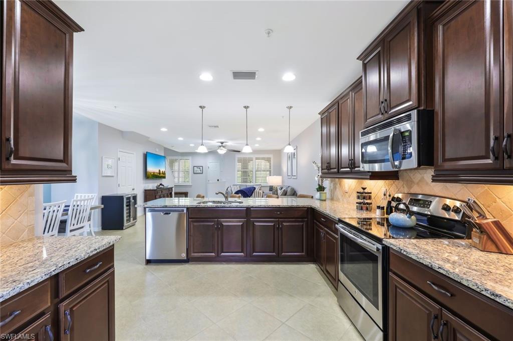 Kitchen featuring backsplash, light stone counters, ceiling fan, stainless steel appliances, and decorative light fixtures