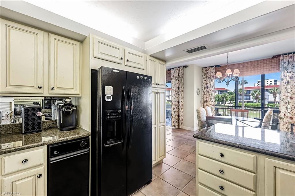 Kitchen featuring cream cabinets, dark stone countertops, black refrigerator with ice dispenser, and light tile patterned floors