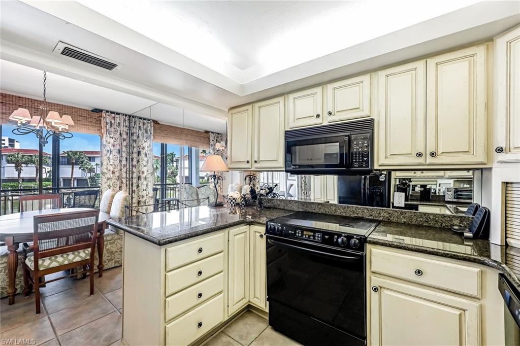 Kitchen with black appliances, a chandelier, kitchen peninsula, cream cabinetry, and light tile patterned floors