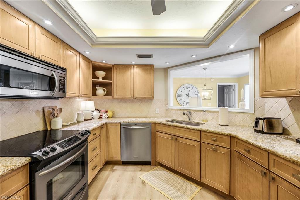 Kitchen featuring appliances with stainless steel finishes, tasteful backsplash, sink, light hardwood / wood-style floors, and a raised ceiling