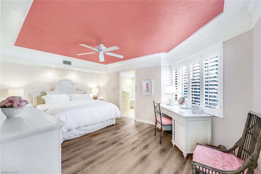 Bedroom with a tray ceiling, ceiling fan, light hardwood / wood-style floors, ensuite bathroom, and ornamental molding