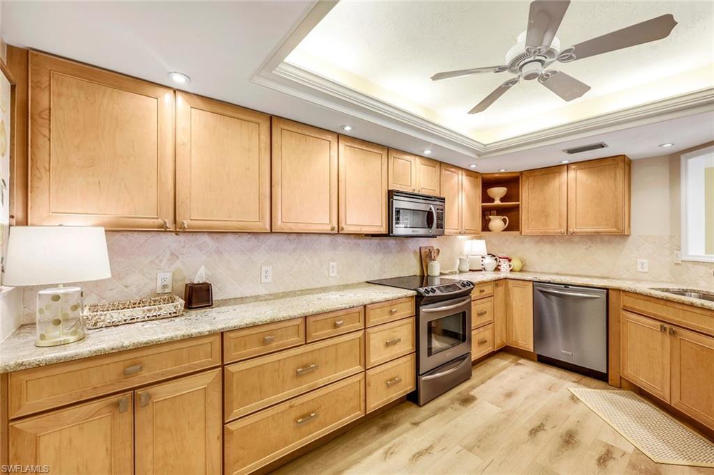 Kitchen featuring stainless steel appliances, light stone counters, decorative backsplash, light wood-type flooring, and ceiling fan