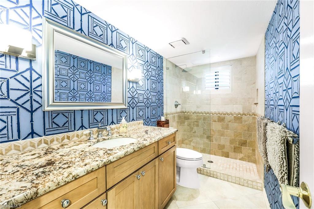 Bathroom featuring tiled shower, vanity, tile walls, toilet, and tile patterned flooring