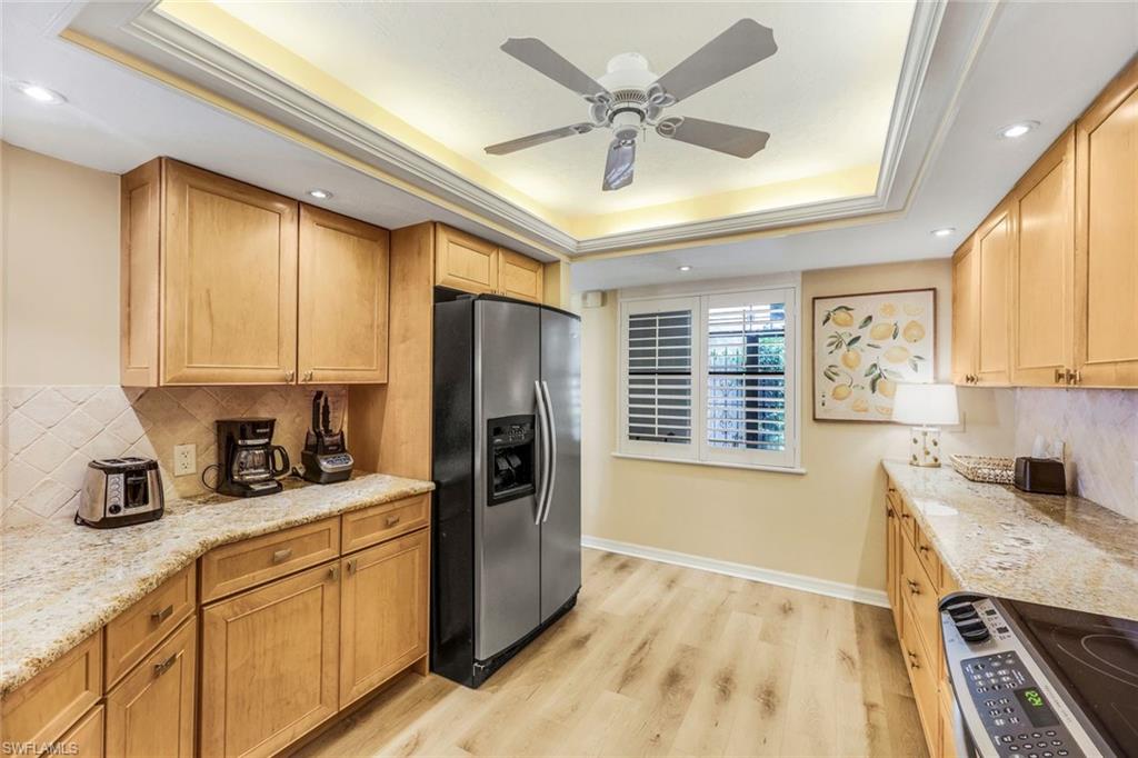Kitchen featuring light hardwood / wood-style flooring, light stone countertops, stainless steel fridge with ice dispenser, and a tray ceiling