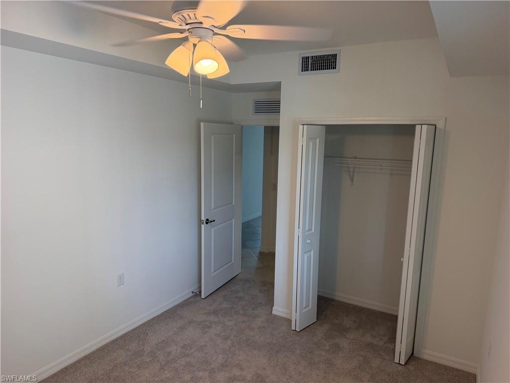 Carpeted room featuring a ceiling fan with integrated lighting, bi-fold closet doors, a paneled interior door, and white baseboards