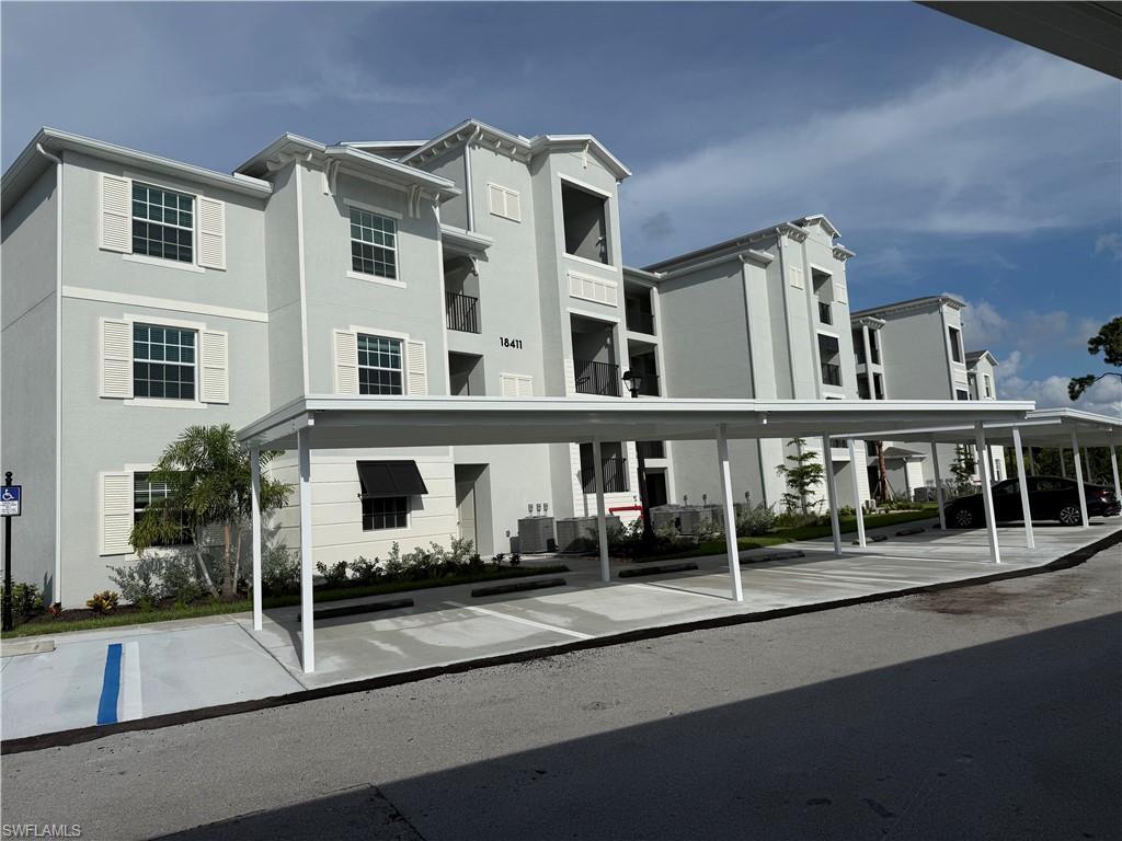 Multi-story residential building featuring light grey stucco exterior, white window shutters, and a covered parking structure