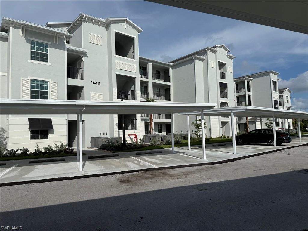 Multi-story building featuring light grey stucco facade, decorative white window shutters, and multiple balconies with dark railings