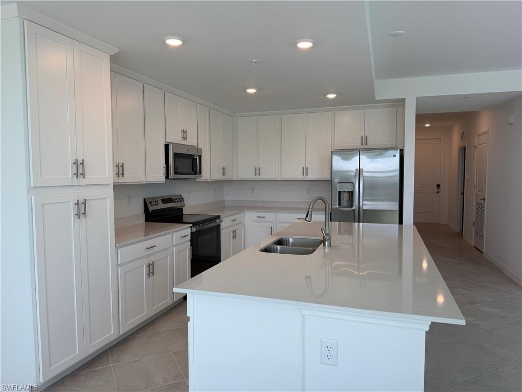Modern kitchen featuring white shaker cabinetry, stainless steel appliances, a large center island with a double sink, light-toned countertops, and recessed lighting