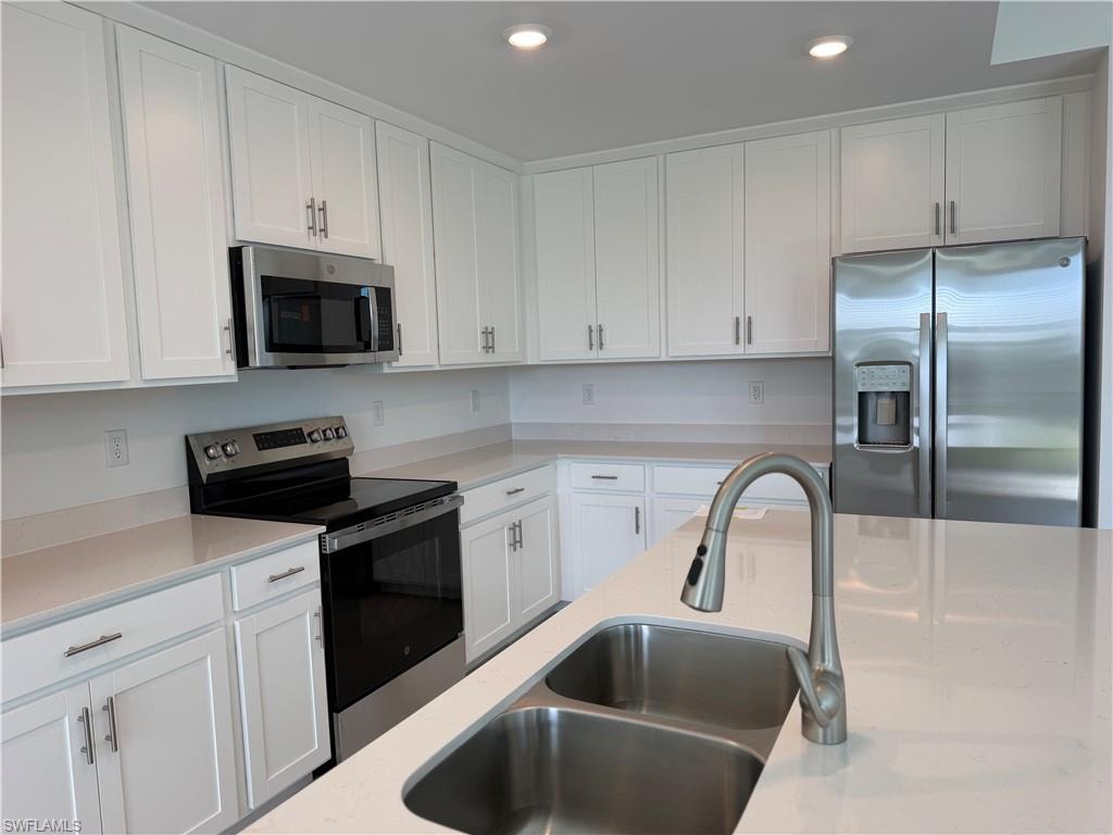 Contemporary kitchen featuring white shaker cabinetry, stainless steel appliances, light-toned countertops, and a double basin sink with a pull-down faucet