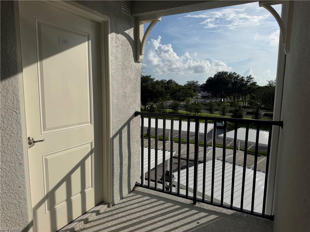 Balcony featuring a black wrought iron railing, textured exterior wall finish, and a paneled exterior door with brushed nickel hardware