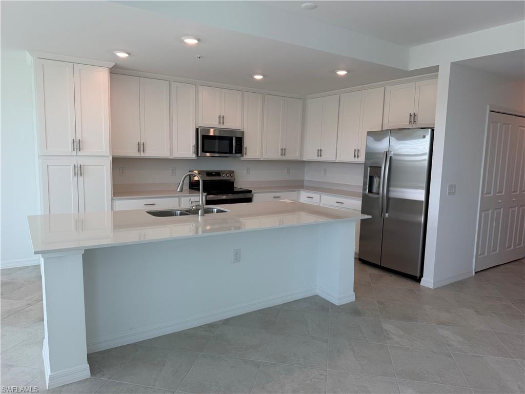Modern kitchen featuring white shaker cabinetry, stainless steel appliances, a large center island, light-toned countertops, and tile flooring
