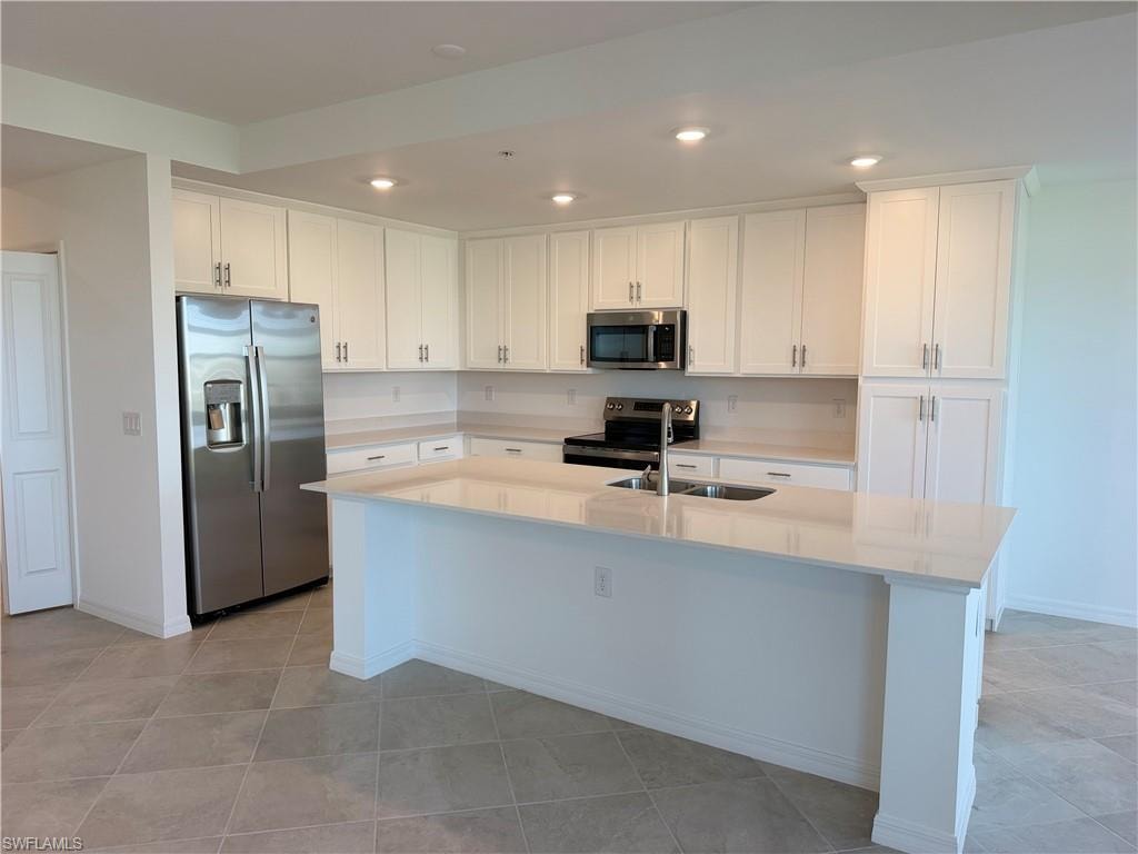 Kitchen featuring a center island with a stainless steel undermount sink, white cabinetry, integrated stainless steel appliances, light-toned countertops, and tile flooring