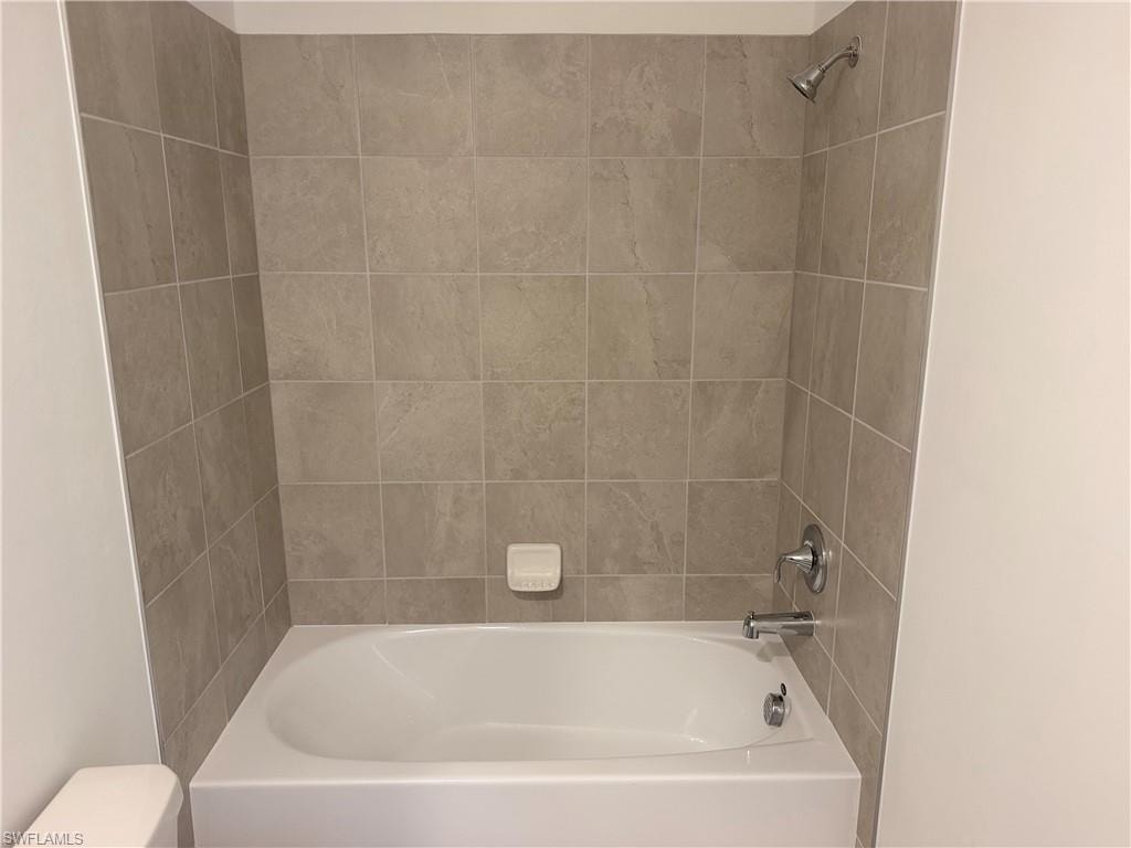 Bathtub and shower combination featuring neutral-toned wall tiles, chrome fixtures, and a white porcelain tub