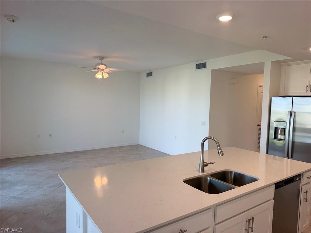 Kitchen island featuring a dual-basin stainless steel sink with a high-arc brushed nickel faucet, a quartz countertop, and white shaker-style cabinetry