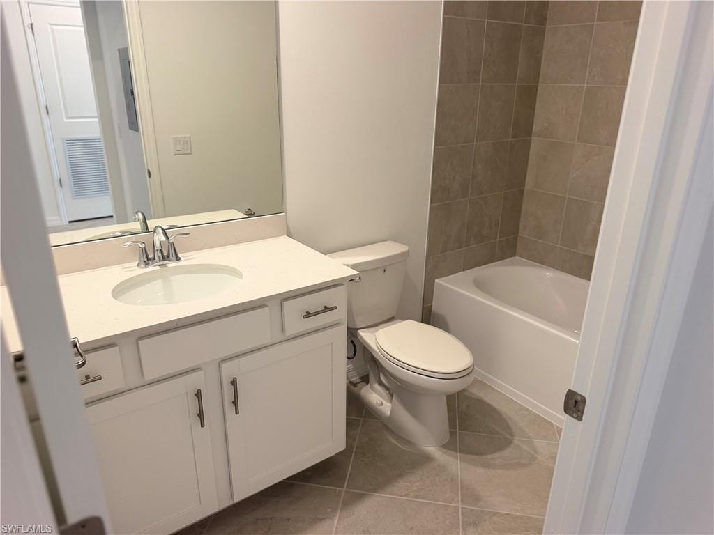 Bathroom featuring a white vanity with an undermount sink, a chrome faucet, a large mirror, a white toilet, a white bathtub, and light-toned tile flooring