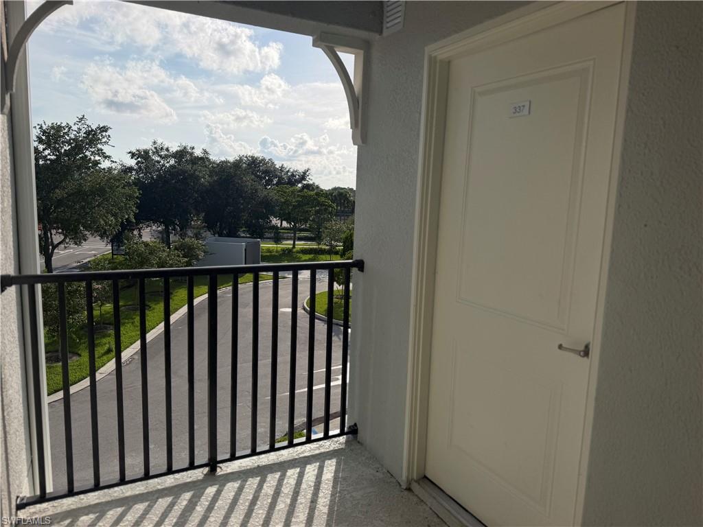 Balcony with black metal railing, offering a perspective of the surrounding paved road and mature trees