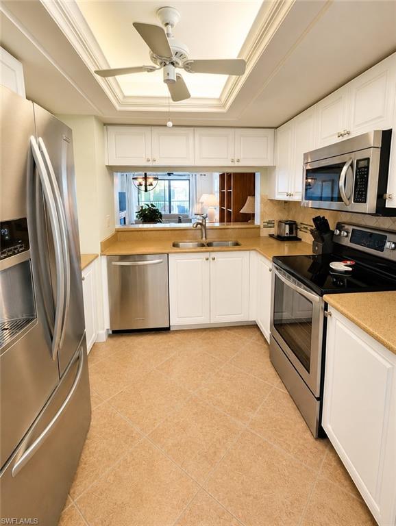 U-shaped kitchen featuring white cabinetry, stainless steel appliances, a pass-through window, light-colored countertops, and tiled flooring