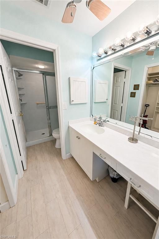 Bathroom featuring a light-toned wood-finish flooring, a white vanity with integrated sink, a large wall-mounted mirror, a ceiling fan with light, and a shower enclosure with sliding glass doors