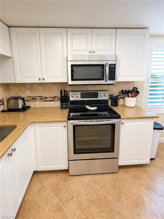 Kitchen featuring stainless steel appliances, light-toned countertops, white cabinetry with silver hardware, a tiled backsplash, and tile flooring