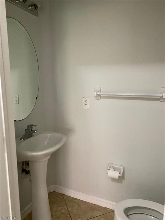 Pedestal sink with chrome faucet, oval mirror, and tile flooring