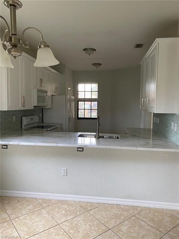 Kitchen featuring bright white cabinetry, a marble-finish countertop with an undermount sink, a glass tile backsplash, and tile flooring