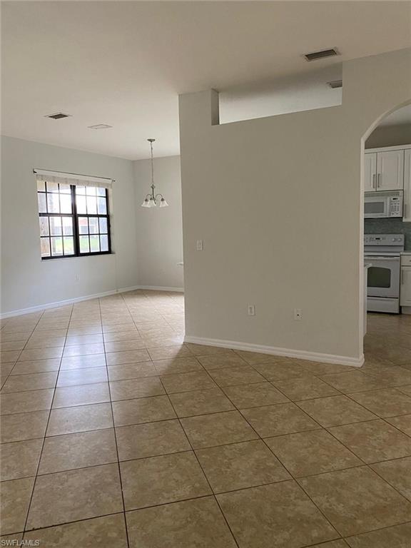 Expansive tiled flooring spans the open living area, featuring a multi-pane window with blinds and a hanging chandelier