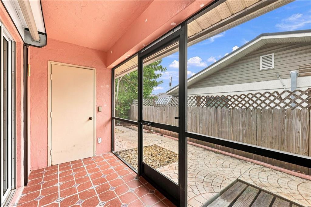 Screened patio featuring terracotta-toned tile flooring with geometric patterns, textured coral-colored walls, and a white exterior door