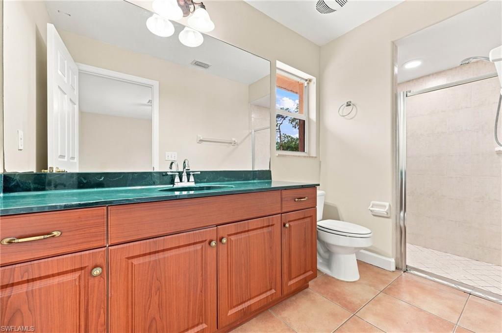 Spa-inspired primary bathroom showcasing warm wood cabinetry with ample storage, a striking turquoise countertop, dual sink configuration, and a spacious walk-in shower with tile surround and frameless glass enclosure