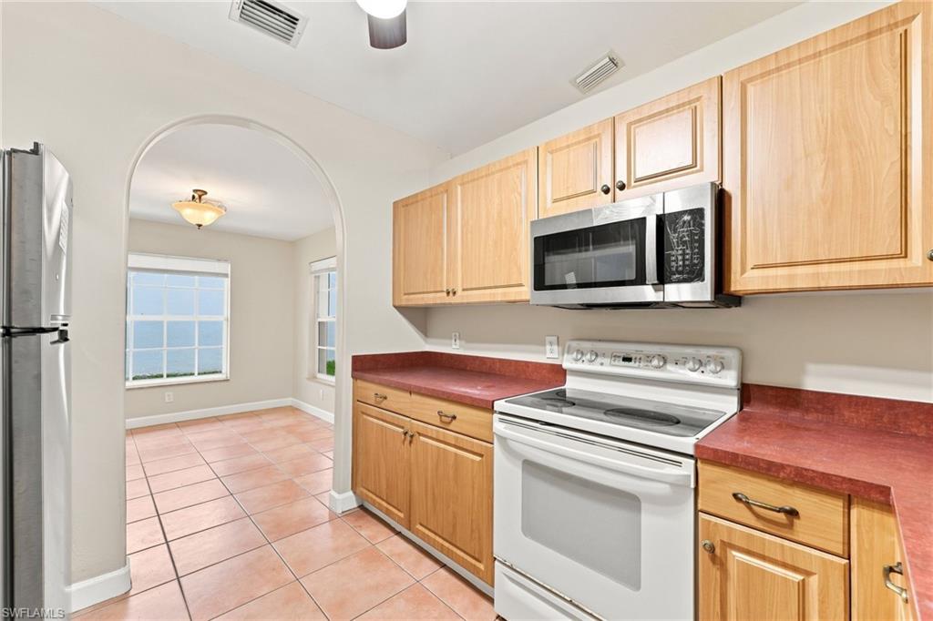 Galley kitchen featuring wood cabinetry with brushed nickel hardware, stainless steel appliances including a microwave and electric range, tile flooring, and a burgundy laminate countertop