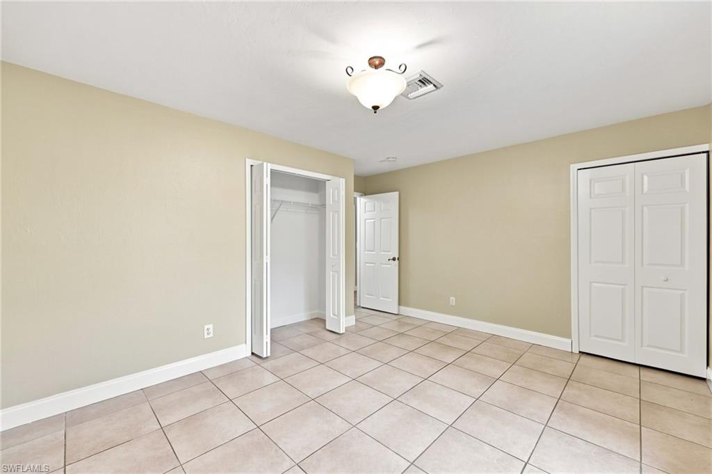 Spacious bedroom featuring neutral wall finishes, tile flooring throughout, and abundant natural light from multiple windows
