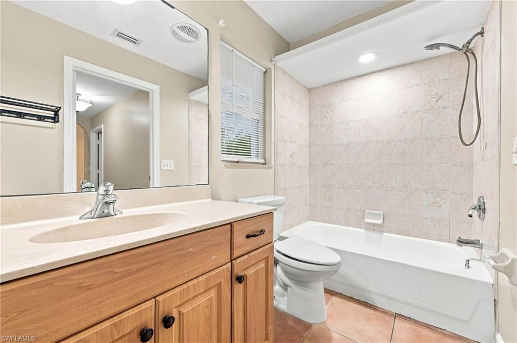 Full bathroom featuring a wood-finish vanity with an integrated sink, a large mirror, and a tiled shower/tub combination with a handheld showerhead