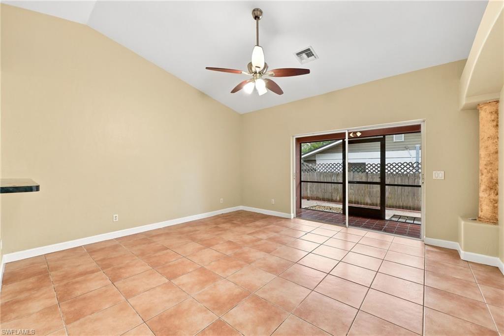 Vaulted ceilings enhance this room featuring tile flooring, a ceiling fan, and sliding glass doors leading to a screened patio