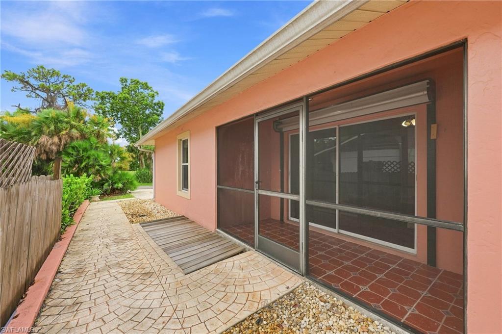 Coral stucco exterior with expansive covered patio featuring sliding glass doors, terracotta tile flooring, and metal-frame screening